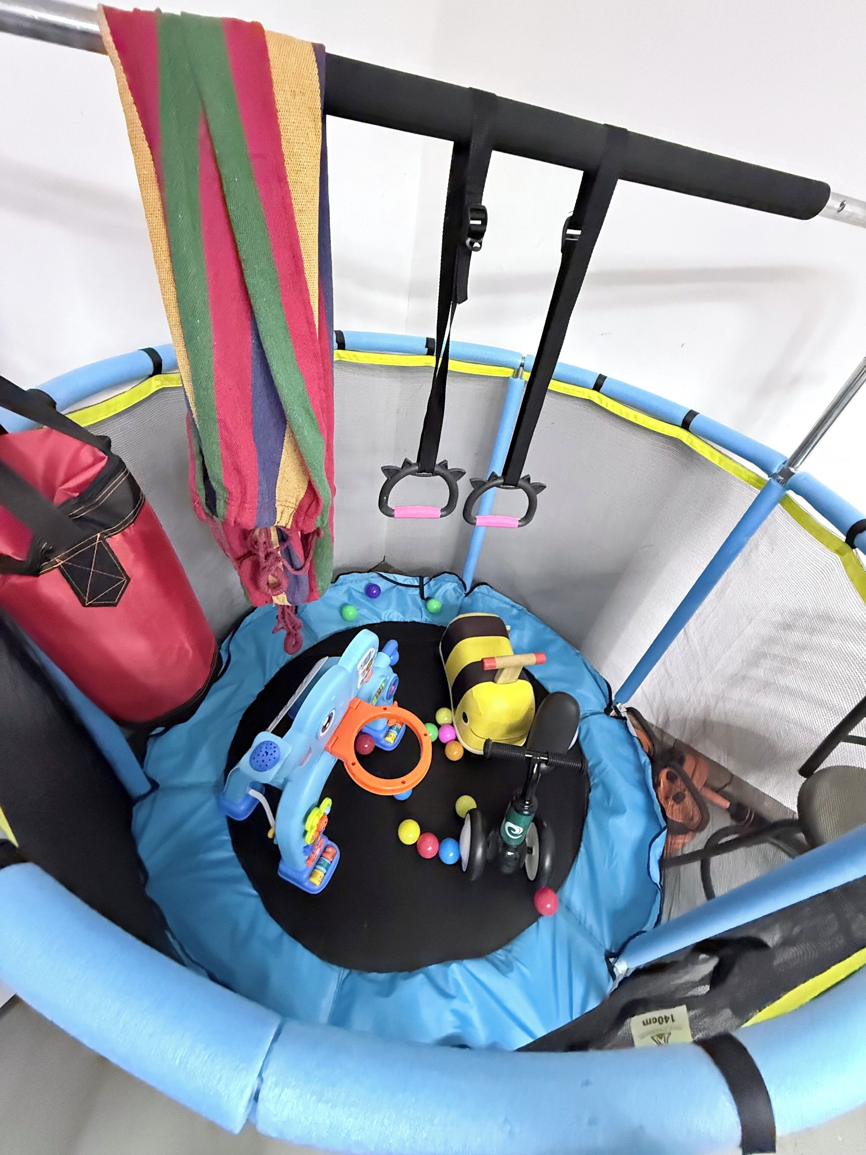 A trampoline with safety bars, a red bag, and various toys.