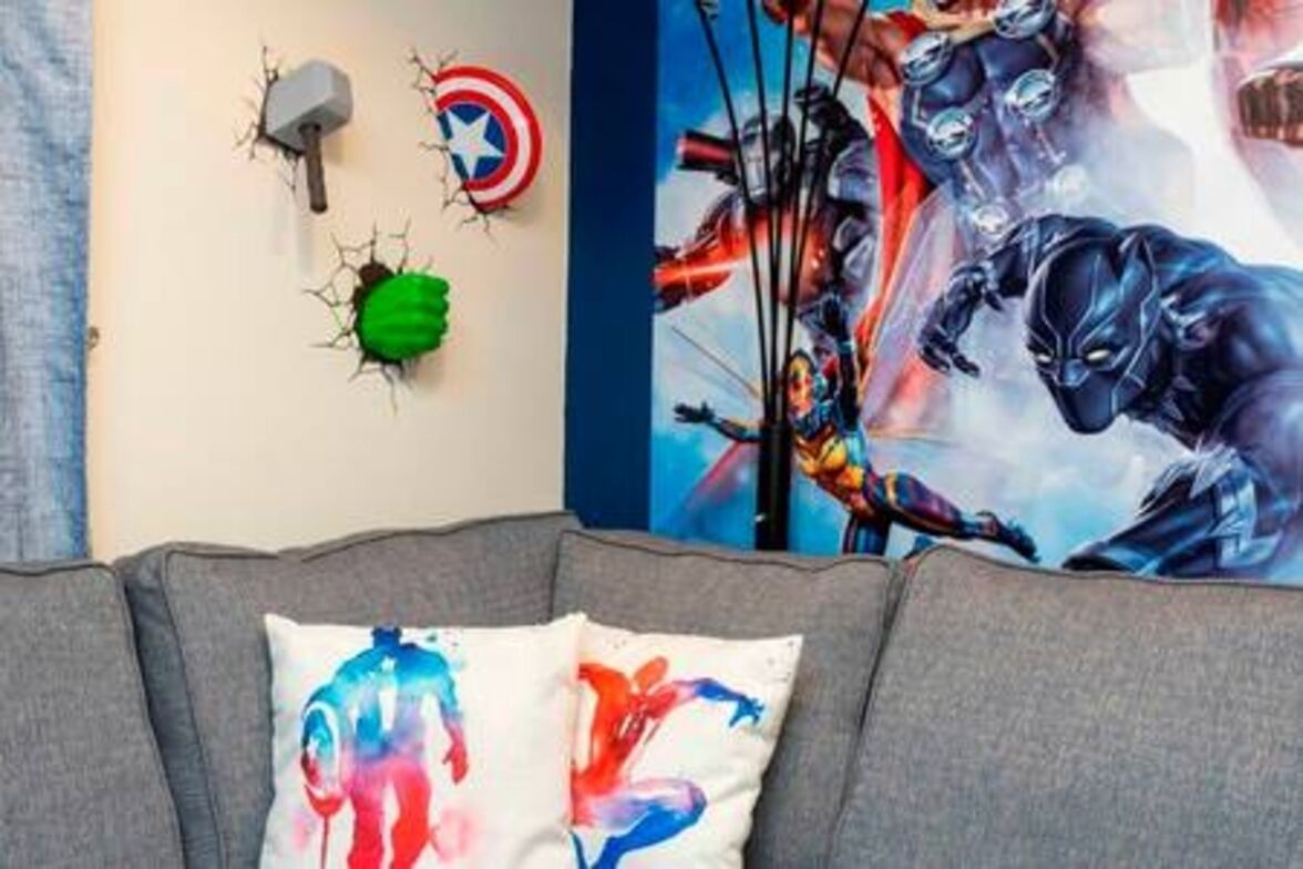 Un soggiorno con un divano grigio, uno scudo di Captain America e un pugno verde decorativo appeso al muro.