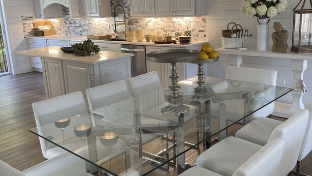 A modern kitchen with white cabinetry, a glass dining table, and white chairs.