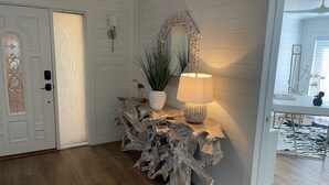 A wooden console table with a lamp and decorative items, a mirror, and a door with a decorative glass panel.