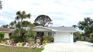 A single-story house with a garage, surrounded by a well-maintained garden with various plants and a palm tree.