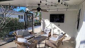 An outdoor patio with wicker furniture, a ceiling fan, and a TV mounted on the wall.