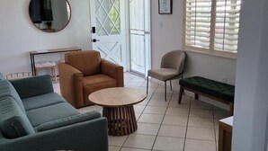 A living room with a sofa, armchairs, a coffee table, and a bench. There is a door with glass panels and a window with blinds.
