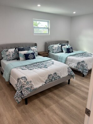 A bedroom with two beds, each with patterned bedding, a small window, and a wooden floor. - Home with pool - walk or bike to beach! (Naples)