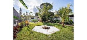 A backyard with a concrete fire pit, surrounded by grass and various plants. - Home with pool - walk or bike to beach! (Naples)