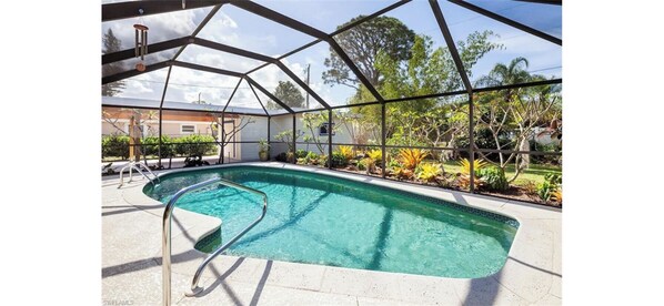 A swimming pool with a glass enclosure, surrounded by plants and trees. - Home with pool - walk or bike to beach! (Naples)