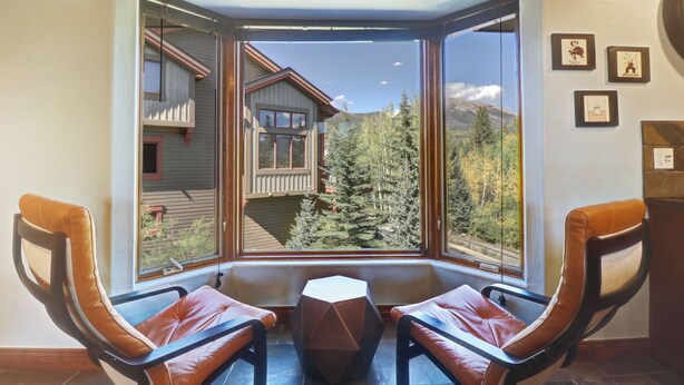 Il s'agit d'une chambre d'angle dotée d'une grande fenêtre donnant sur une montagne et des arbres. On y trouve deux fauteuils en cuir et une petite table.