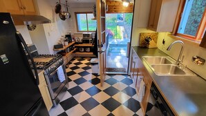 A kitchen with a black and white checkered floor, wooden cabinets, a refrigerator, a stove, a sink, and a window overlooking a garden. - Spot On The Hill (Seattle)