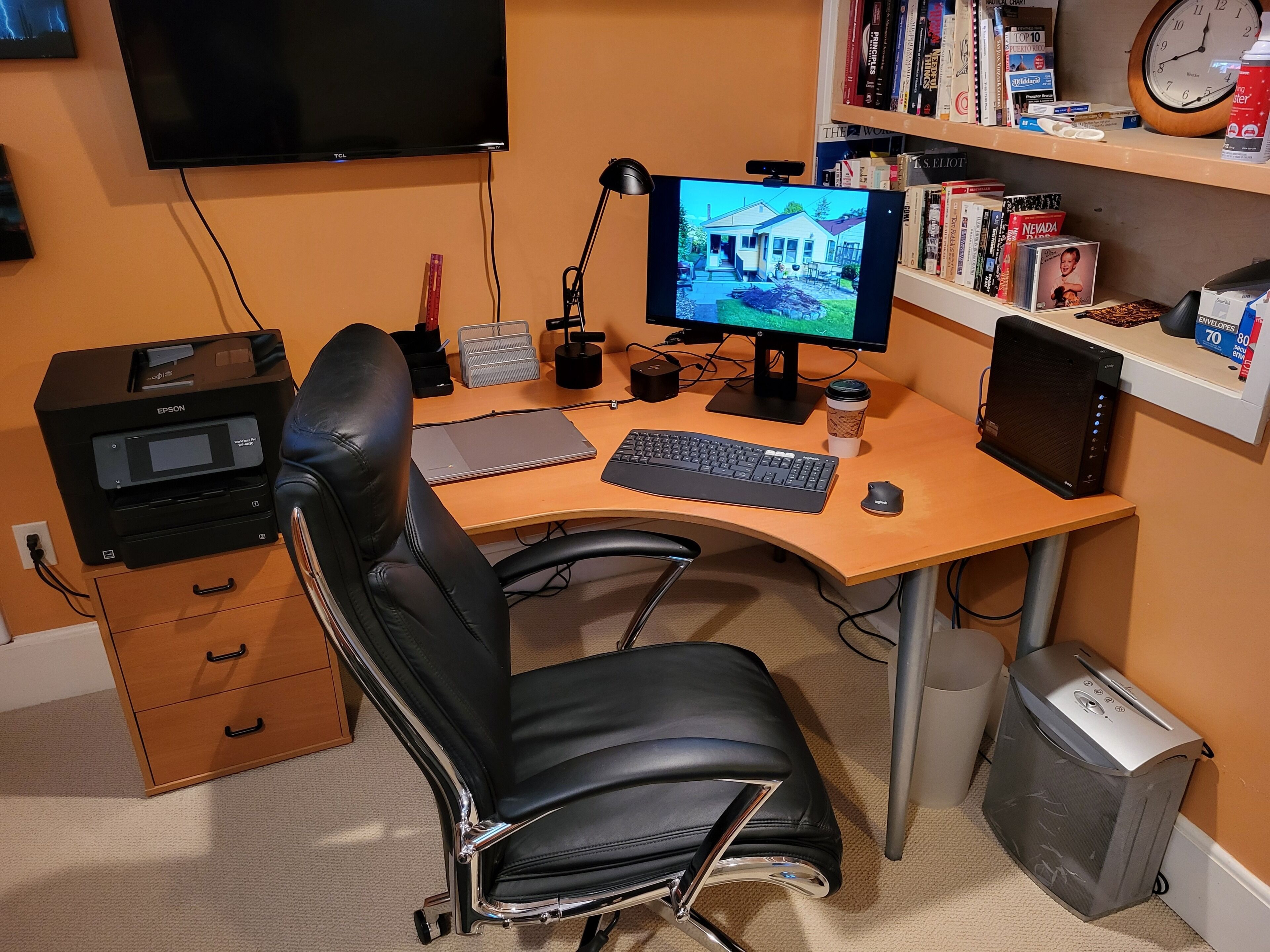 A home office with a desk, chair, computer, monitor, bookshelf, and a TV.