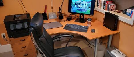 A home office with a desk, chair, computer, monitor, bookshelf, and a TV.