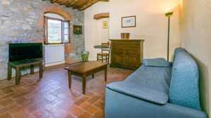 A cozy living room with a stone wall, wooden ceiling beams, a television, a sofa, a table, and a fireplace.