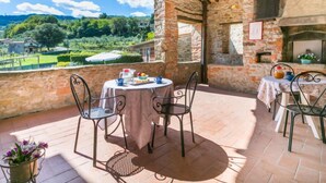 A terrace with stone walls, a round table with chairs, and a view of a green landscape.