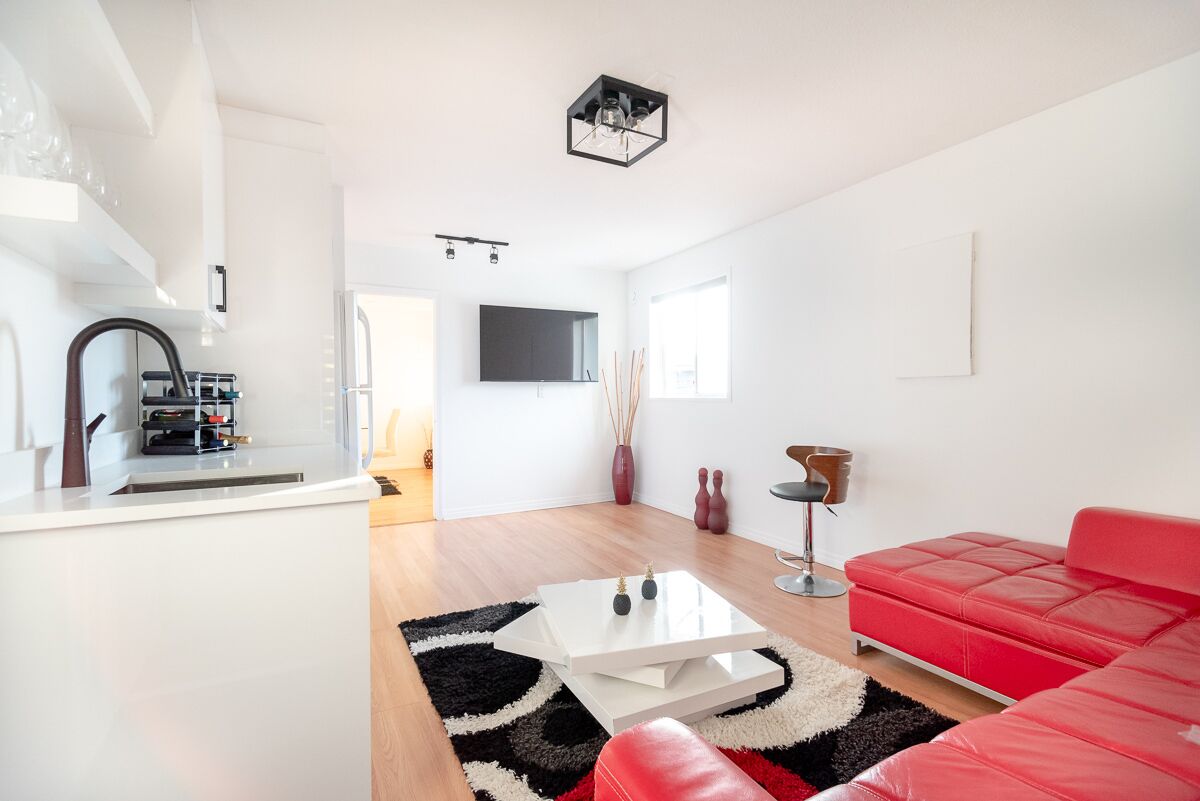 A modern living room with a red sofa, a white coffee table, and a kitchen area with a white countertop and a black backsplash.