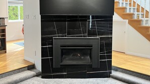 Una cocina moderna con chimenea de mármol negro, techo de madera y una escalera al fondo.