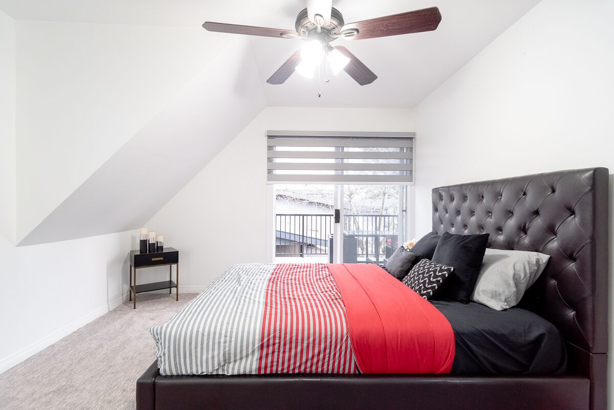 A bedroom with a bed, a ceiling fan, a window with blinds, and a nightstand with candles.