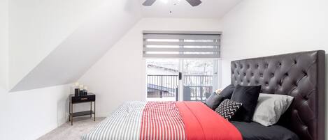 A bedroom with a bed, a ceiling fan, a window with blinds, and a nightstand with candles.