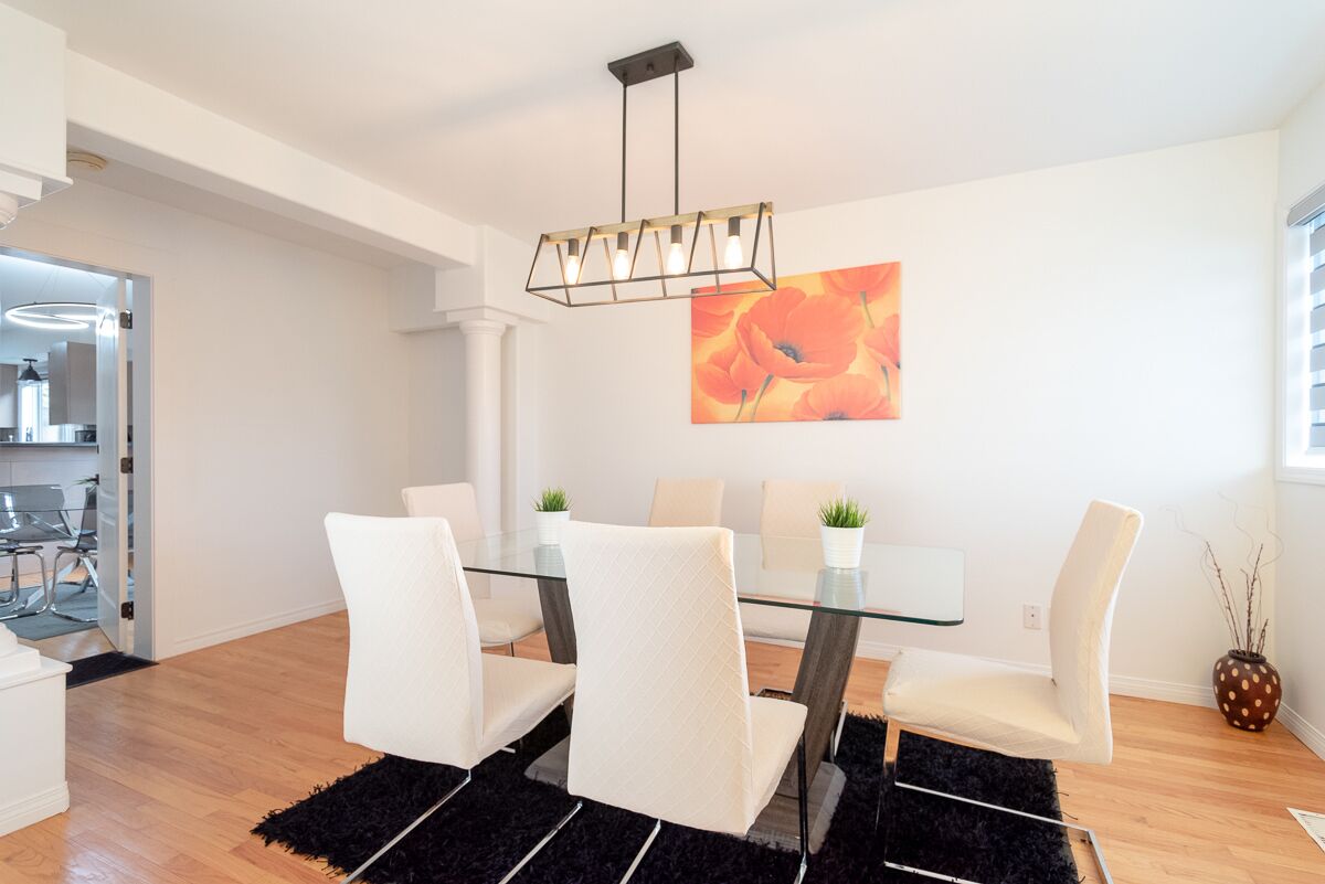 A modern dining area with a glass table and white chairs, a black rug, and a painting on the wall.