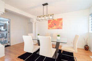 Un espace repas moderne avec une table en verre et des chaises blanches, un tapis noir et un tableau au mur.