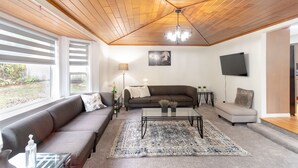 Una sala de estar moderna con techo de madera, un ventanal grande, un sofá, una mesa de centro y una televisión.