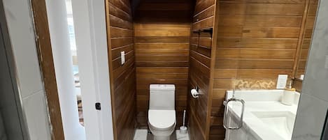 A compact bathroom with wooden paneling, a toilet, a sink, and a shower area.