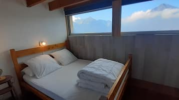 A bed with a wooden headboard and two pillows, a bedside table with a lamp, and a window with a mountain view.