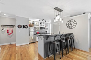 Una cocina moderna con una isla central, taburetes de bar, un refrigerador de acero inoxidable y un microondas.