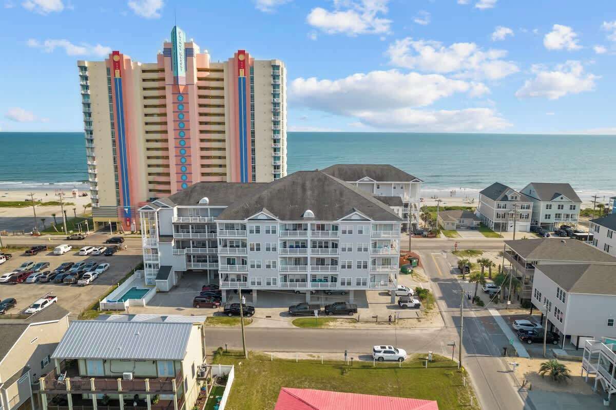 A multi-story hotel with a parking lot, a swimming pool, and a view of the beach and ocean.