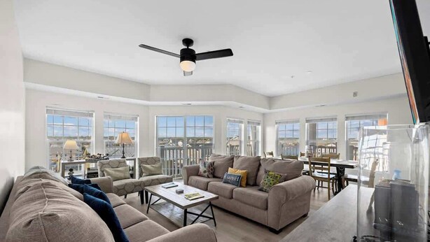 A spacious living room with a high ceiling, large windows, and a ceiling fan. - Channel Views! 6 Bedroom Spacious Deluxe Condo (north myrtle beach)