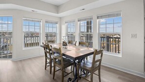A spacious dining area with a large table and chairs, large windows with a view, and a balcony. - Channel Views! 6 Bedroom Spacious Deluxe Condo (north myrtle beach)