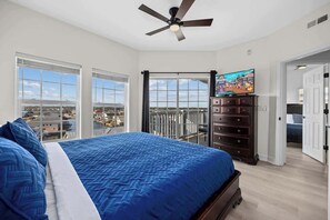 Quarto com cama grande, ventoinha no teto, televisão e varanda com vista para a cidade.