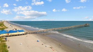A beach with a pier extending into the water, a sandy beach, and a building with a blue roof. - Channel Views! 6 Bedroom Spacious Deluxe Condo (north myrtle beach)