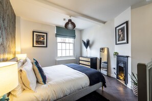 A modern bedroom with a large bed, a dresser, a fireplace, and a window with a view.