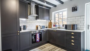 A modern kitchen with dark cabinetry, a stainless steel range hood, a built-in oven, and a window providing natural light. - The Book Club, York. (York)