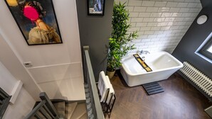 A modern bathroom with a freestanding bathtub, a large potted plant, and a staircase leading to another level. - The Book Club, York. (York)