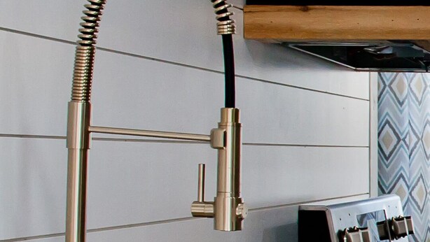 A kitchen with a stainless steel sink, a gold-colored faucet with a flexible hose, and a wooden ceiling.