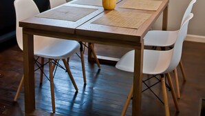 A dining area with a wooden table, white chairs, and a yellow vase.