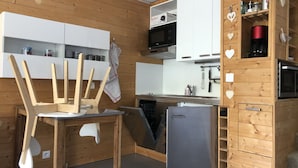 Une cuisine compacte avec des murs en bois, un four à micro-ondes encastré et un petit réfrigérateur.