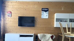 Une pièce avec un téléviseur fixé au mur, un mur en bois, un panneau indiquant une destination de voyage et une affiche représentant une piste de ski.