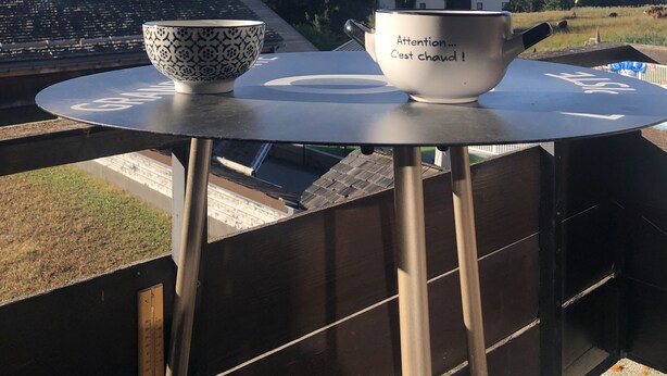 Une table sur laquelle se trouvent un bol blanc et une théi ère blanche ornée de motifs, le tout placé devant un paysage montagneux.