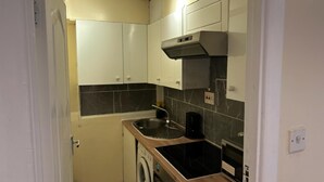 Una cucina compatta con mobili bianchi, forno integrato, microonde e lavatrice.