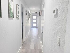 Um corredor com paredes brancas, piso de madeira e quadros nas paredes.