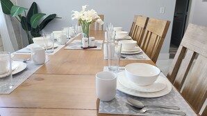 Ein Esstisch ist gedeckt mit weißen Tellern, Schüsseln, Tassen und Besteck, und in der Mitte steht eine Vase mit weißen Blumen.