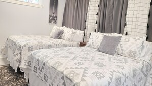 Ein Schlafzimmer mit zwei Betten, gemusterten Textilien, einem Fenster mit Blick und einem Wandbild.