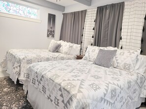 Quarto com duas camas, roupa de cama estampada, janela com vista e um quadro na parede.