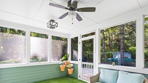 A sunroom with a green lawn, a wicker sofa, and a ceiling fan.