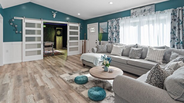 A spacious living room with a grey sofa, teal walls, and a wooden floor.