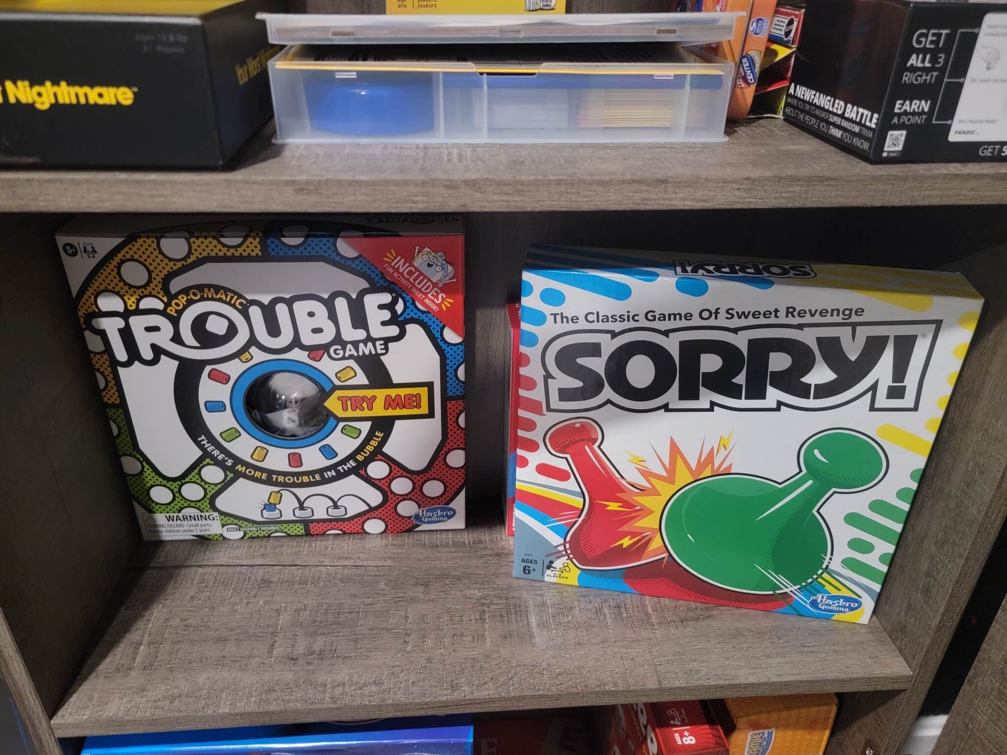 Twee gezelschapsspellen, 'Trouble Game' en 'Sorry!', staan op een plank.