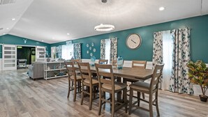 A spacious dining area with a wooden table and chairs, teal walls, and a clock on the wall.