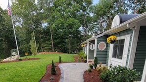 A pathway leading to a house with a green exterior, surrounded by a landscaped garden with various plants and flowers.