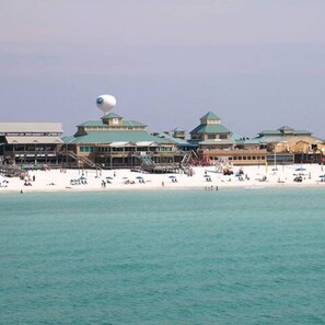 A beachfront hotel with multiple green-roofed buildings, a sandy beach, and a clear view of the ocean.